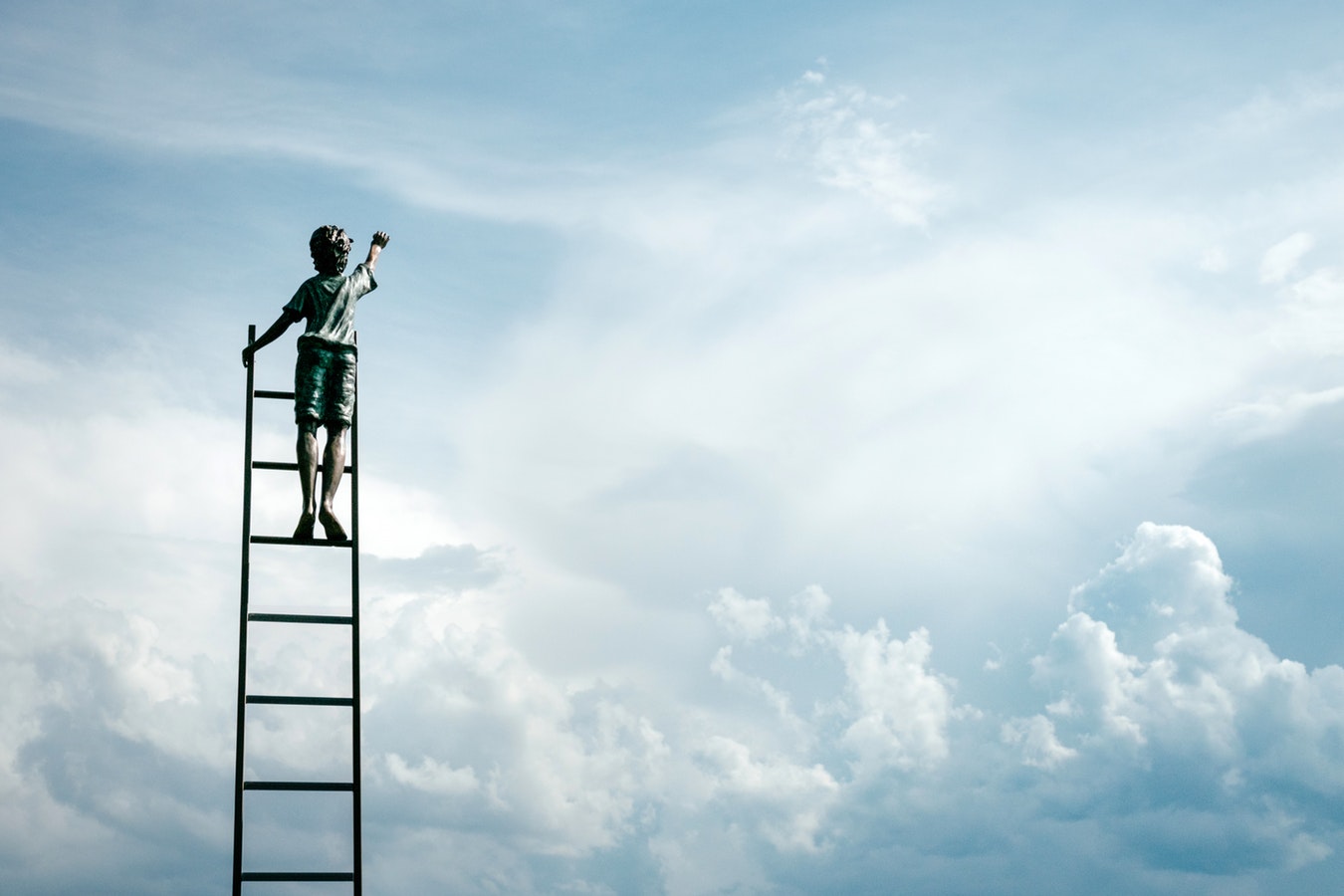 Image of a boy on a ladder reaching for the sky